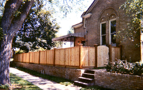 Capped Privacy Fence with Bulky Posts Curved Top Gate and Brick Retaining Wall